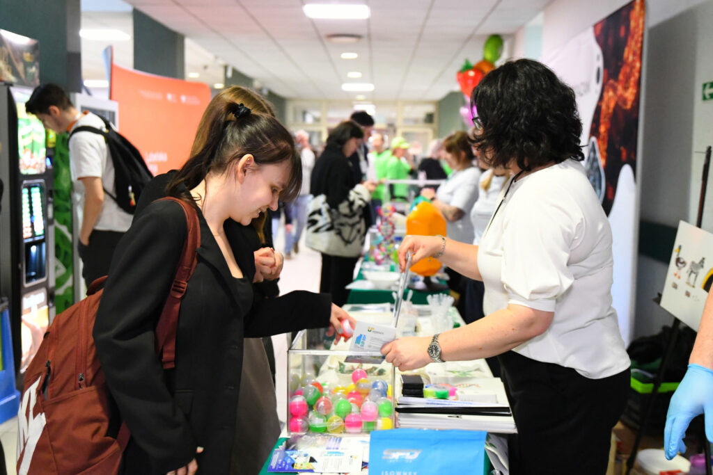 uczennica przygląda się stoisku; z przezroczystego pudełka wybiera kolorowy okrągły pojemnik