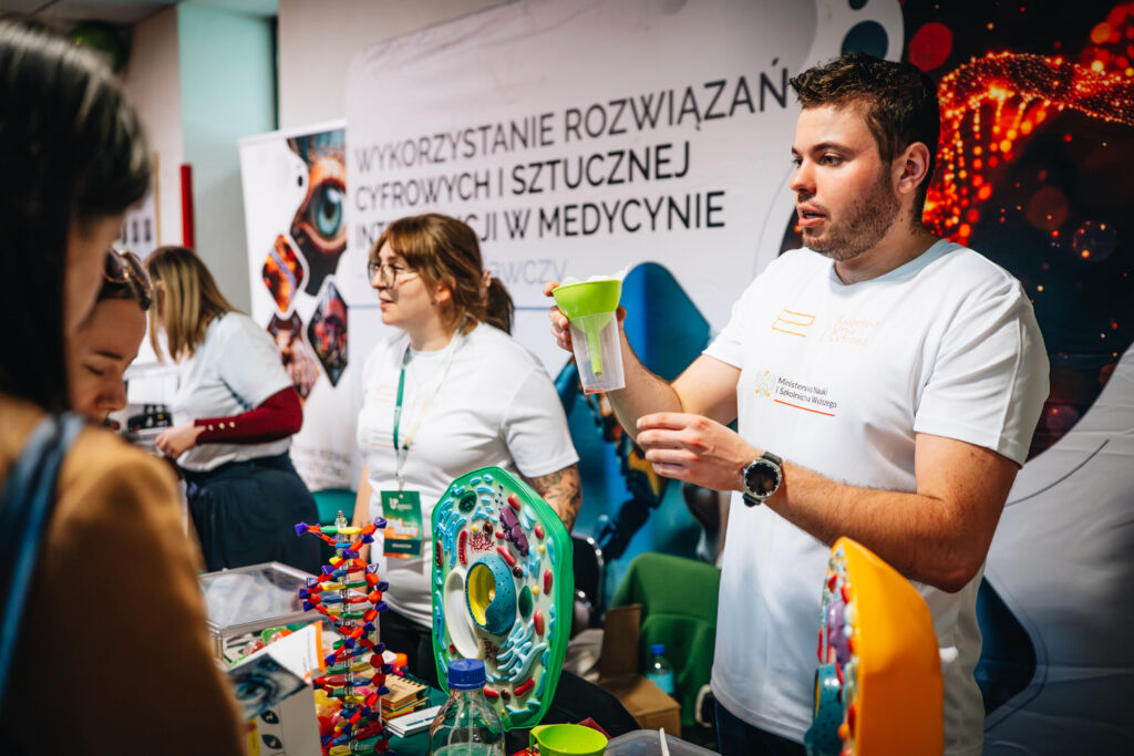 mężczyzna prezentuje eksperyment, w dłoniach trzyma lejek i szklany pojemnik